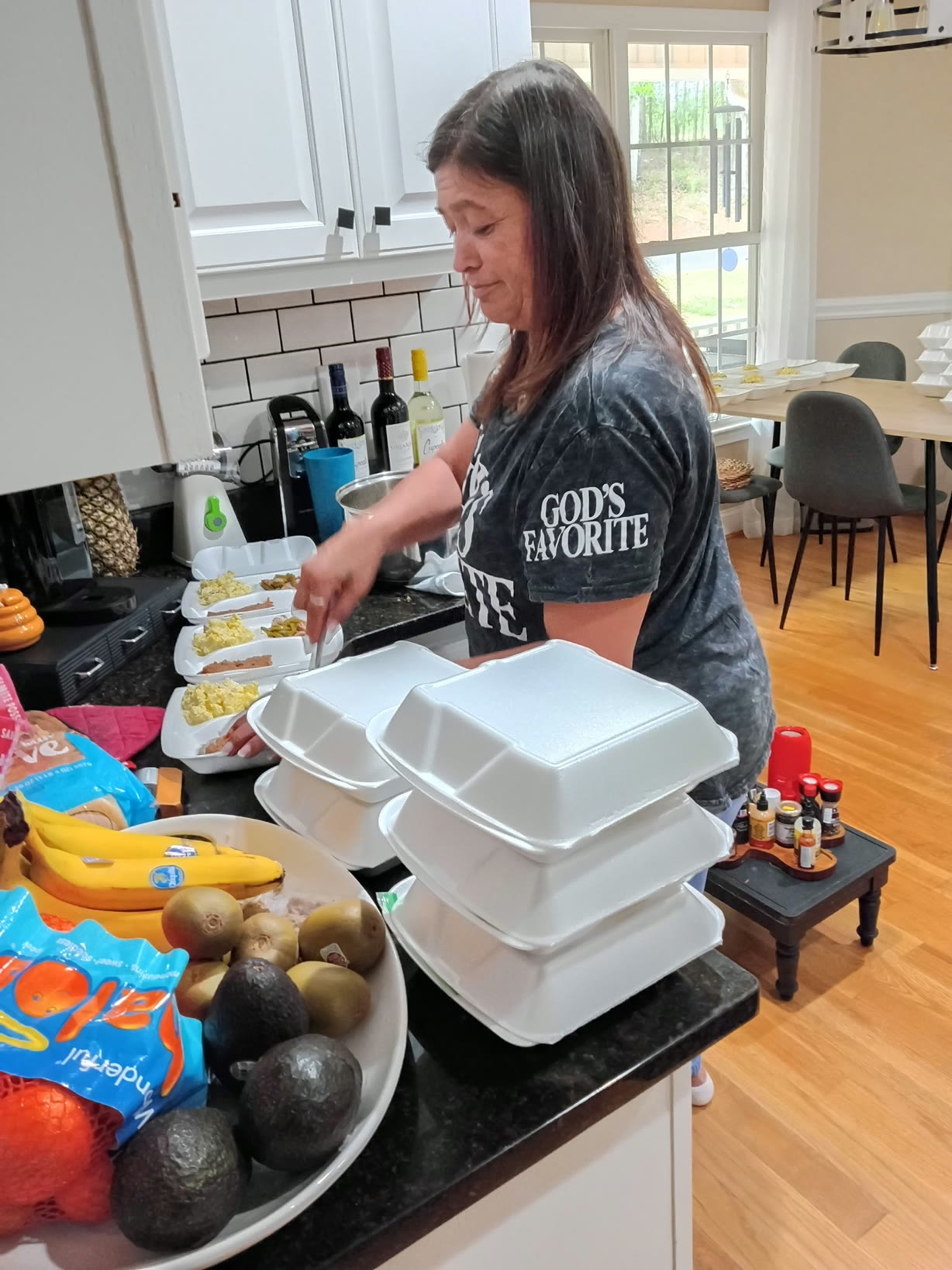Tracy preparing a row of open meal containers in a kitchen